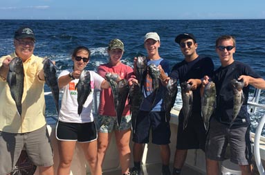 A man, 2 teenage women and 3 teenage men each hold up 2 sea bass and smile for the camera