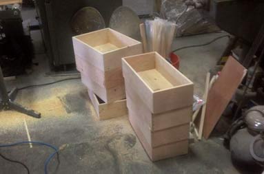 Newly cut and assembled wooden drawers, stacked and sitting on ground.