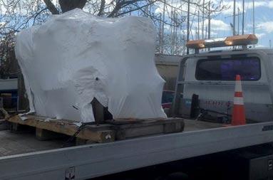 The old Detroit engined covered in white shrink wrap, mounted on the back of a flatbed truck being transported to its new owners