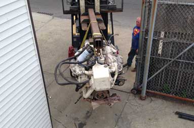 The engine is lower to ground level as one of the guys from T&S Marine waits to guide it