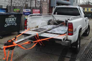 Rear view of a truck in the middle of the street driving away as it carries the long shaft from the boat