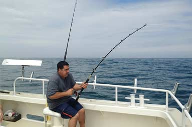 David sitting on the boat with line in water fighting a fish