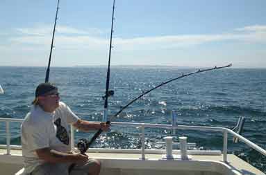 Frank sitting on the boat with line in water fighting a fish