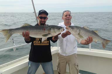 Two guys stand next to each other holding up their catch.
