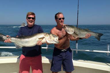 Two other guys on the boat each smiling, holding up the large bass they caught