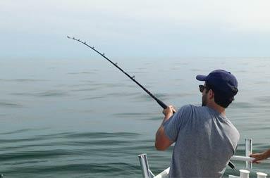View of the back of one of the guys reeling in a fish from the boat