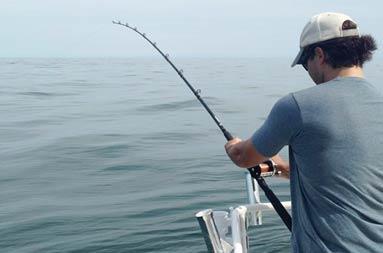 View of the back of another one of the guys reeling in a fish from the boat
