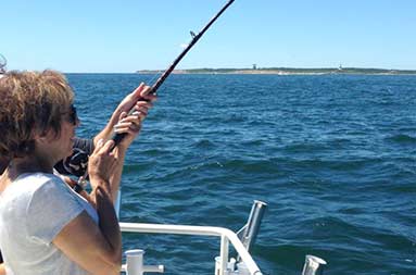 Capt. Jill standing next to her mom, helping her reel in a fish
