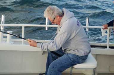 One of the guys, Alan, sitting down on the boat reeling in his catch.