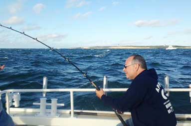 One of the guys, Steve, sitting down on the boat reeling in his catch.