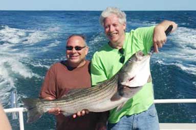 Two of the guys, Alan and Steve, standing on the boat holding up the bass they caught.