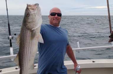 One of the guys on the trip smiling into the camera and holding up a jumbo sea bass