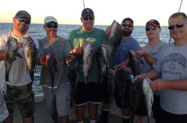 An early evening shot of the group of guys all holding their catch and smiling