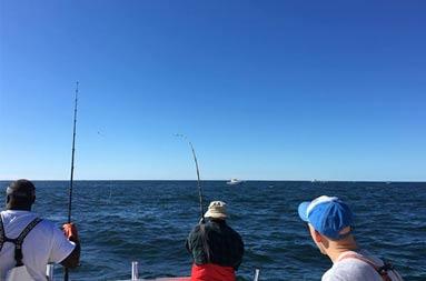 View from the cabin of the back of the boat of first mate, Gil, and two men waiting with their reel in the water for a bite.