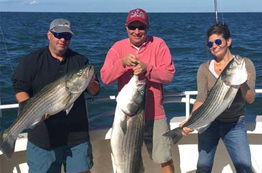 A woman and two men smile as they pose with their catch on the boat.