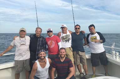 Eight middle-aged and senior men stand on the boat smiling in a group shot.