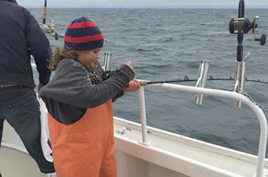 A young boy holds tightly onto his rod as he reels in his catch.