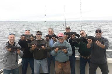 A group of 8 men each hold up the blackfish they caught.