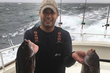A man wearing a fleece holds up the blackfish (tautog) he caught.