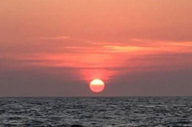 The dark vast ocean at the bottom. Right above the horizon, the rising sun in a reddish/orange sky.