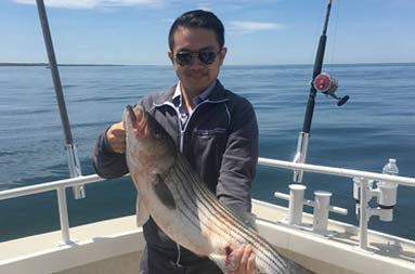 A man aboard the boat holding the striped bass he caught.