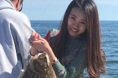 A woman aboard the boat holding the fluke she caught.