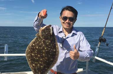 A man aboard the boat holding the fluke he caught.