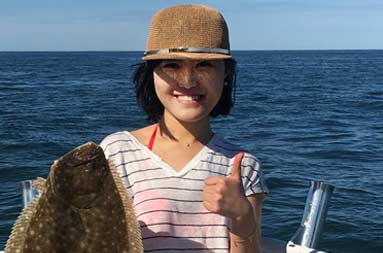 A woman aboard the boat holding the fluke she caught giving a thumbs up.