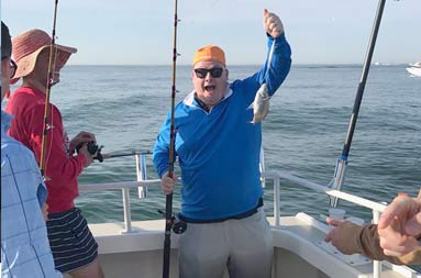 A man aboard the boat holding up a very small fish he caught.