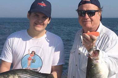 A father and son standing side by side holding up the striped bass they each caught.