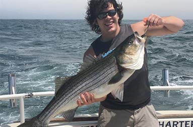 A young man holds up the first striped bass catch of the day.