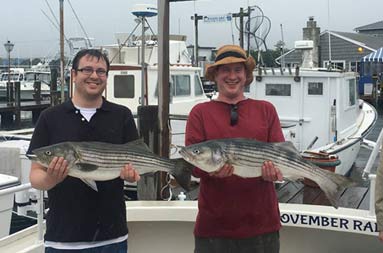 Two men hold up their fish back at the marina in overcast, rainy weather.