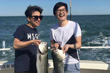 Two young men smile as they each hold up the fish they caught.