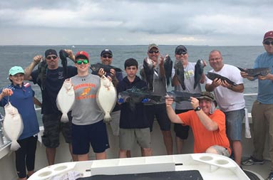 Nine men and boys and a young girl woman hold up the fluke and sea bass they each caught.