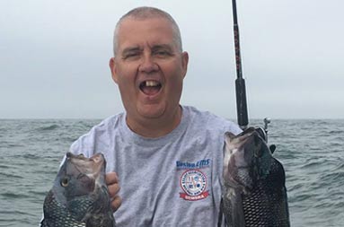 A man holding up two sea bass that he caught.