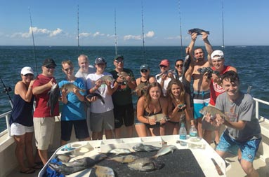 A group of 14 men and woman hold up some the fish they caught, with fish on the fillet table in the foreground.