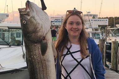 Back at the marina, an adolescent girl stands next to the 45lb fish she caught that's hanging from the scale.