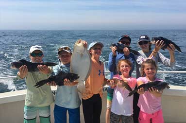 Two adults and 5 children proudly hold up the sea bass and fluke they caught.