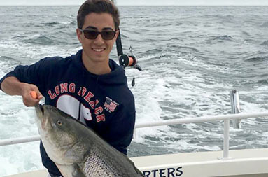 A young man holding up the striped bass he caught.