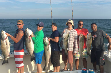 A group of 6 men each smile as they hold up the fish they caught.