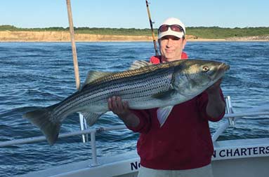 With both hands, a man holds up the striped bass he caught.