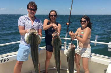 A man and two women all hold up the striped bass they each caught.