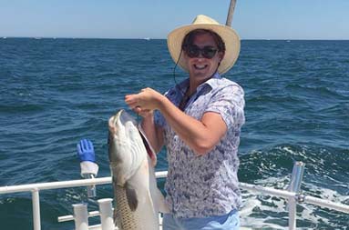 A man smiles as he holds up a striped bass.