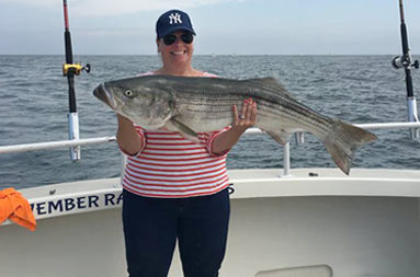 A woman in a long sleeve red and white striped shirt proudly holds up her catch.