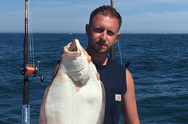 A man, wearing a sleeveless black t-shirt, holds up the fluke he caught.