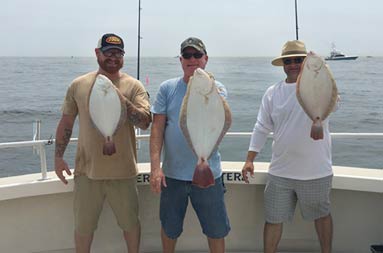Three men each hold up the fluke they caught.