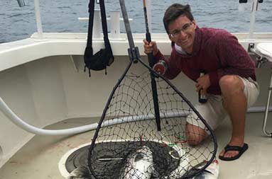 A man kneels down next to 3 striped bass laid out on the floor of the deck.
