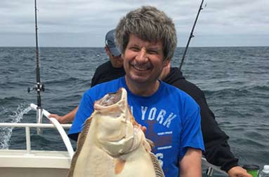A man smiles while holding up the fluke he caught.