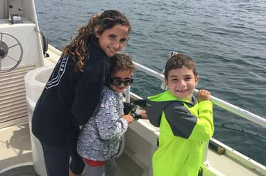 Three children peering over the side of the boat waiting for their catch, look back and smile for the camera.