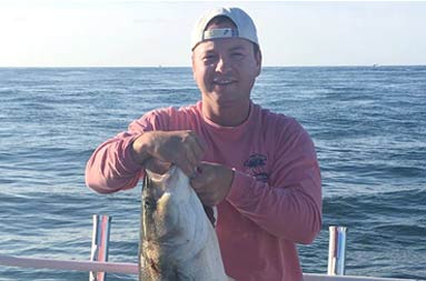 A close up of a man holding up the striped bass he caught